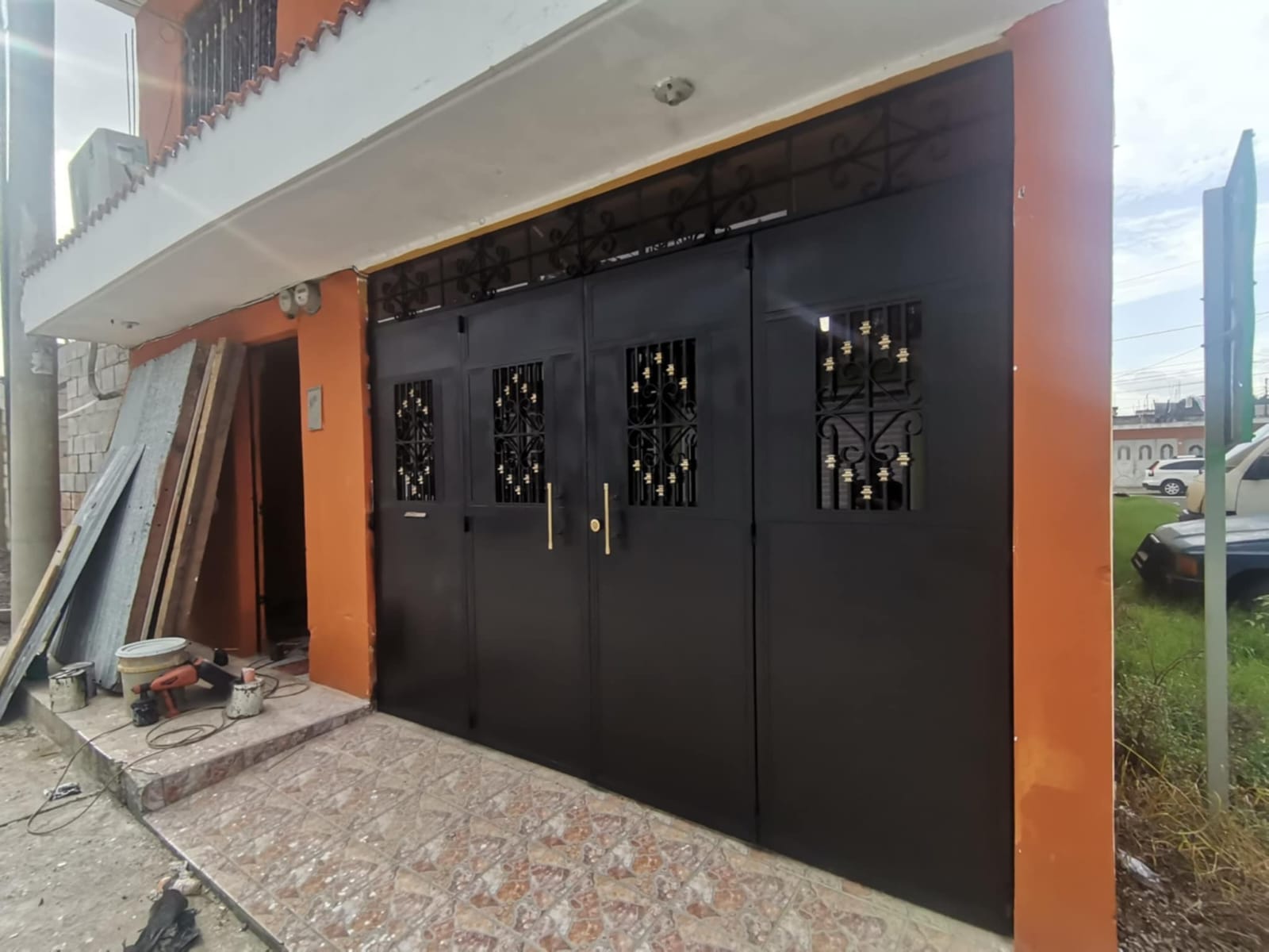 Portón negro de varios paños con detalles ornamentales dorados en fachada naranja