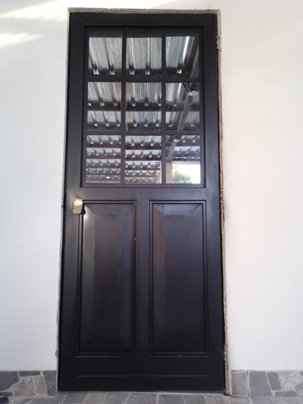 Puerta negra instalada, con paneles inferiores y retícula metálica en la parte superior